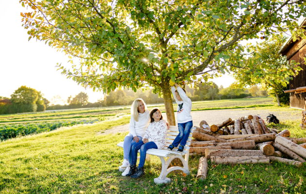 Mary-Ann Schröder mit Kindern unter einem Apfelbaum neben einem Holzstoß